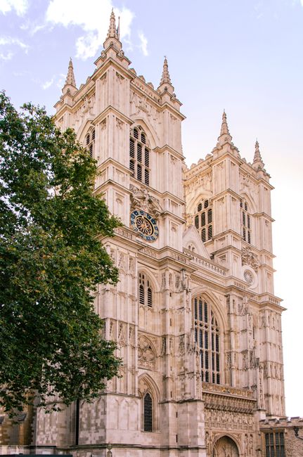 The image shows the front façade of Westminster Abbey, a historic Gothic-style church constructed from light-colored stone with intricate architectural details. Prominent features include two tall, s